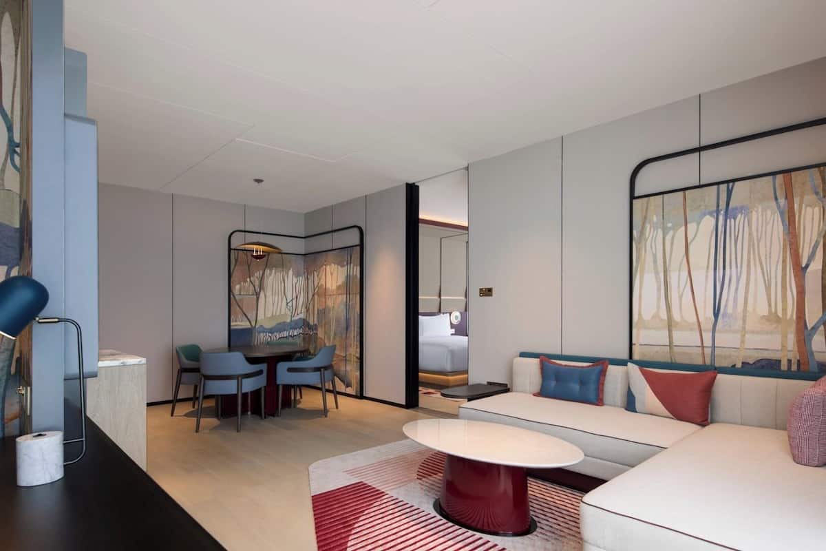 Une chambre d’hôtel moderne avec un canapé, une table ronde, un coin repas avec des chaises et un grand miroir.