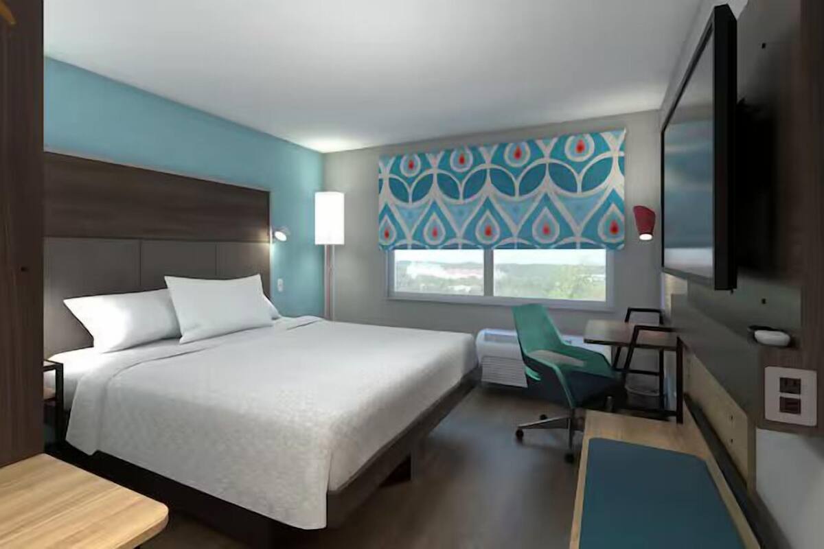 Habitación de hotel con cama, escritorio, silla, televisor y ventana con vistas.
