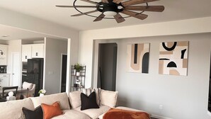 A modern living room with a beige sectional sofa, a wooden ceiling fan, and abstract wall art. - Spacious 7bedroom house in McDonough with Pool, WiFi, fitness room, and theater (McDonough)