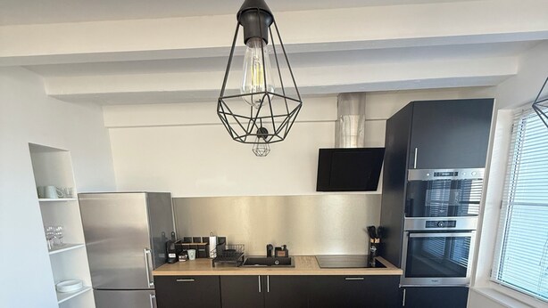 Eine moderne Küche mit schwarzen Schränken, einem Edelstahl-Kühlschrank, einem Einbauofen und einer Pendelleuchte.