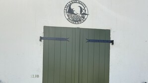 Eine grüne Doppeltür mit Metallbeschlägen und Schloss in einer weißen Wand, darüber ein Fenster.