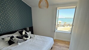 Ein Schlafzimmer mit Bett, einer Hängelampe, einem Fenster mit Blick auf Strand und Steg sowie Holzböden.