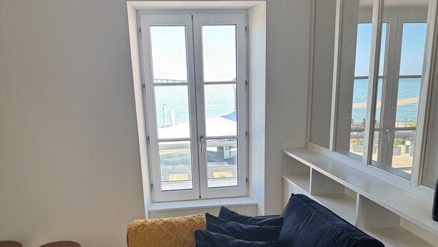 Una sala de estar moderna con un sofá azul oscuro, una mesa de madera y vistas al mar a través de amplios ventanales.