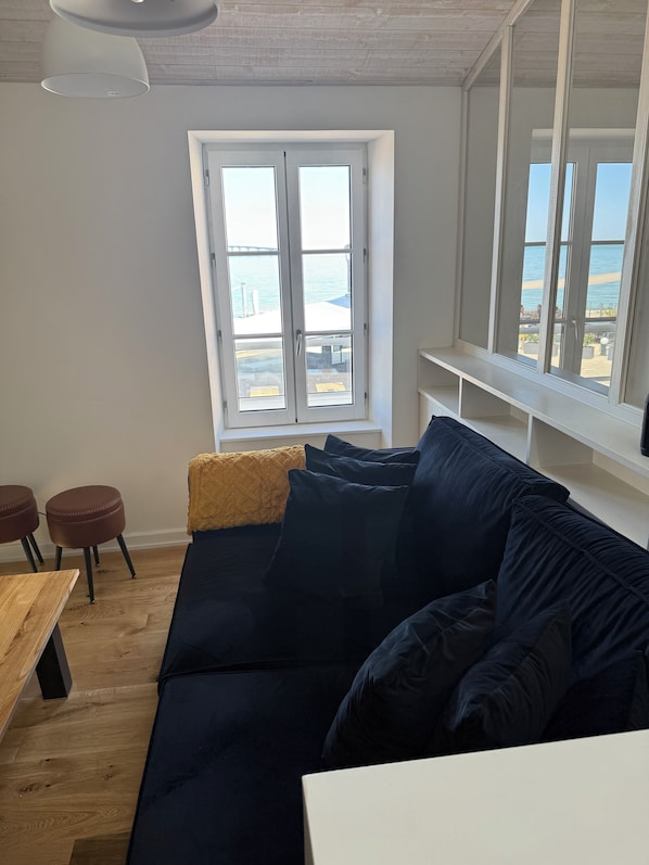 A modern living room with a dark blue sofa, a wooden table, and a view of the sea through large windows. - Villa Raie Manta · Ocean view · Beach steps away (Rivedoux-Plage)