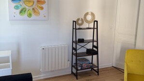 Ein Zimmer mit Holzboden, einer schwarzen Couch, einem gelben Sessel, einem Holztisch, einem Heizkörper, einer weißen Tür und einem Regal mit Dekoration.