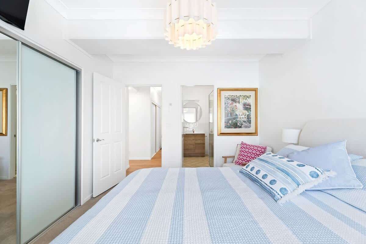Een slaapkamer met een bed, nachtkastje, lamp en een ingelijst schilderij aan de muur.