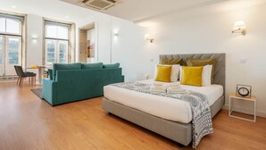 Ein modernes Schlafzimmer mit einem großen Bett, einem türkisblauen Sofa und einem kleinen Tisch mit einer Uhr.