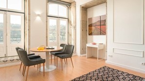 Ein Essbereich mit einem runden Tisch, zwei Stühlen, einer kleinen weißen Kommode und einem Bild an der Wand.