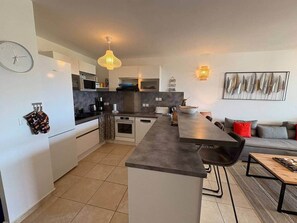Uma cozinha moderna com uma ilha central, armários brancos e uma área de jantar com mesa e cadeiras.