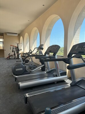 Una palestra con tapis roulant e attrezzature per esercizi, ampie finestre ad arco e vista su spazi verdi.