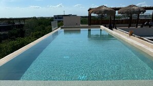 Una piscina infinita rectangular con agua cristalina, rodeada por una terraza de madera y sombrillas de paja.