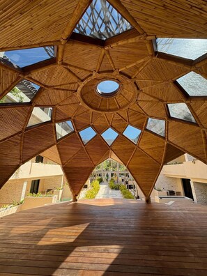 A geometric wooden structure with multiple skylights, leading to a central open area with a view of a building in the background. - Déjá Vu Tulum (Tulum)