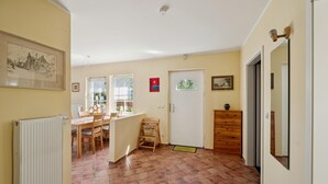 Una habitación con suelo de baldosas, un radiador, una mesa de madera con sillas, un mueble de madera pequeño y una puerta con ventana.