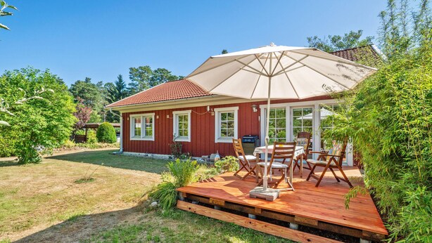 Una casa roja con un patio, muebles de exterior y un gran paraguas.