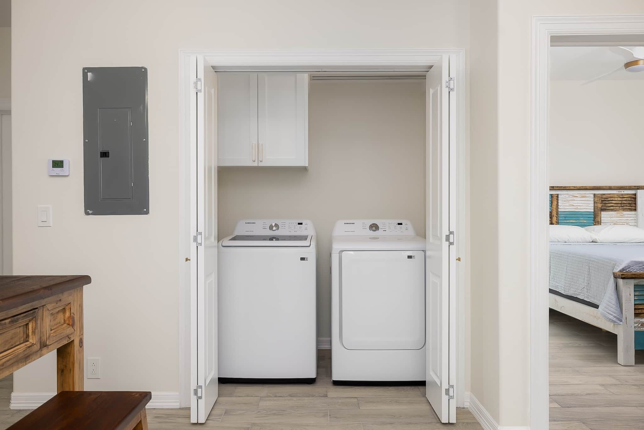 A laundry room with two white front-loading washing machines and a white cabinet above them.