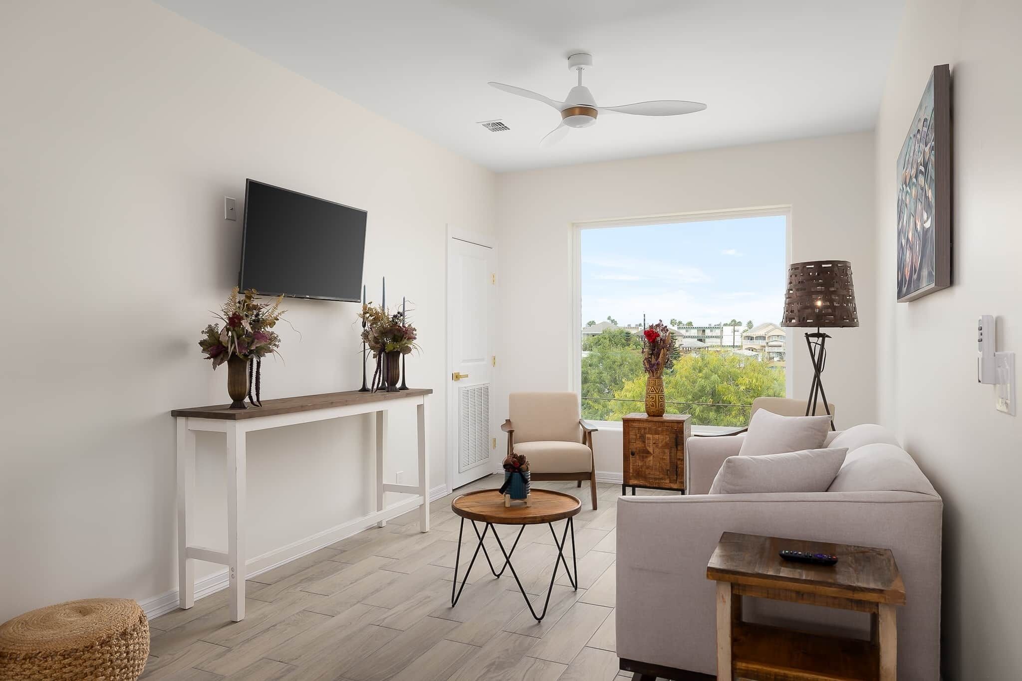 A modern living room with a white sofa, a coffee table, a TV mounted on the wall, and a ceiling fan.