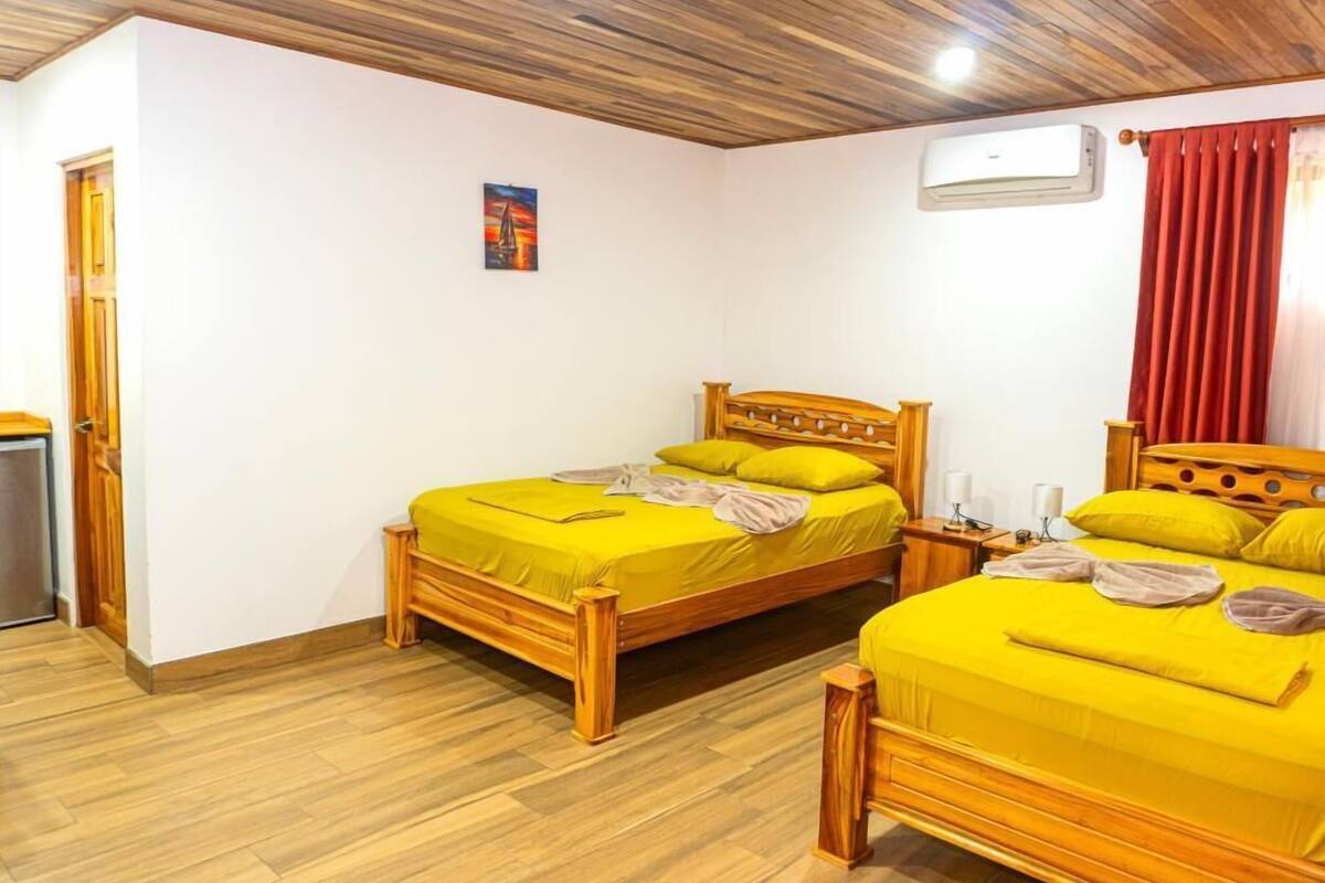 Ein Zimmer mit zwei Holzbettgestellen, einem kleinen Nachttisch, einer Wandklimaanlage und einer Tür.