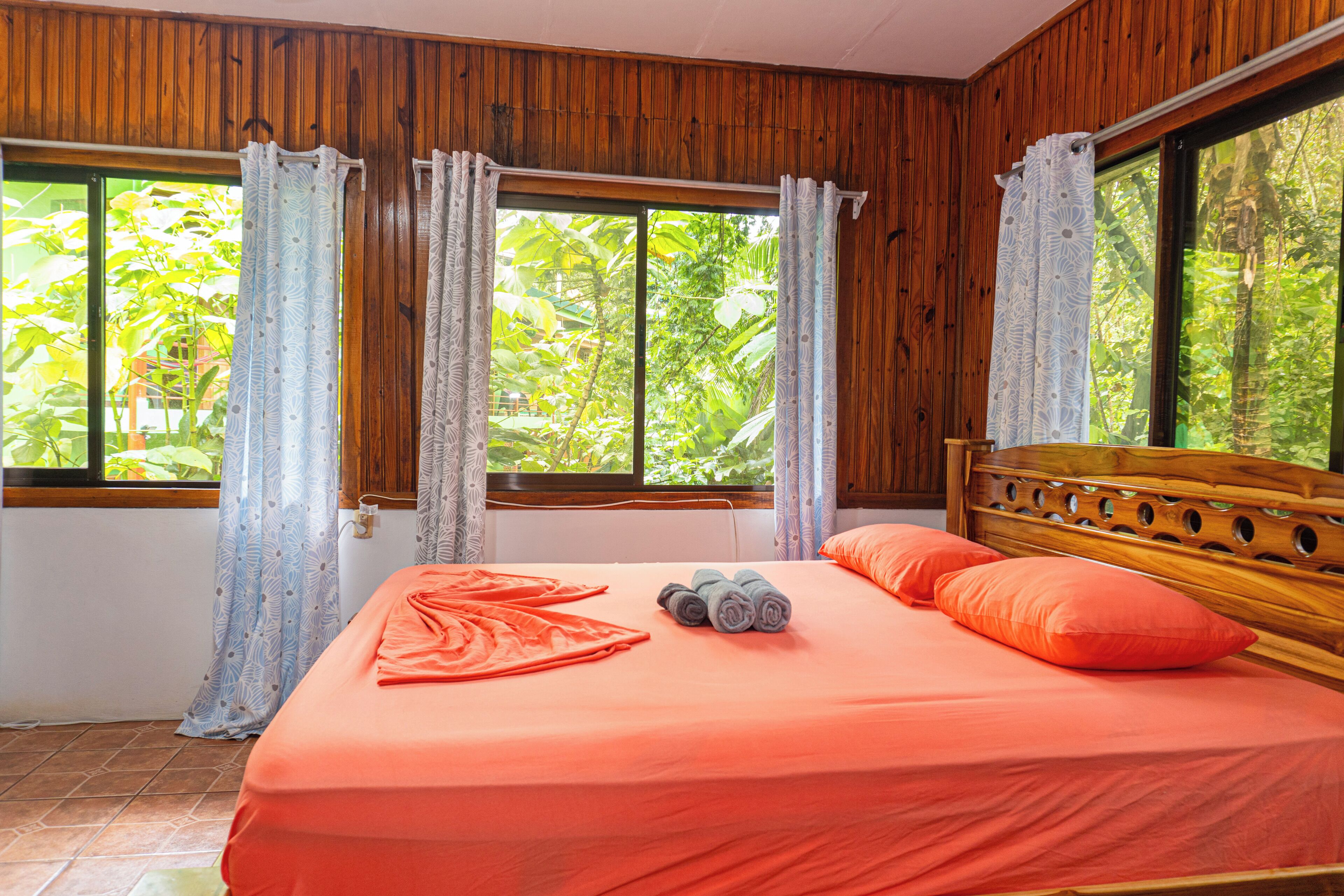 Una habitación con cabecera de madera, cama con colcha naranja y cortinas.