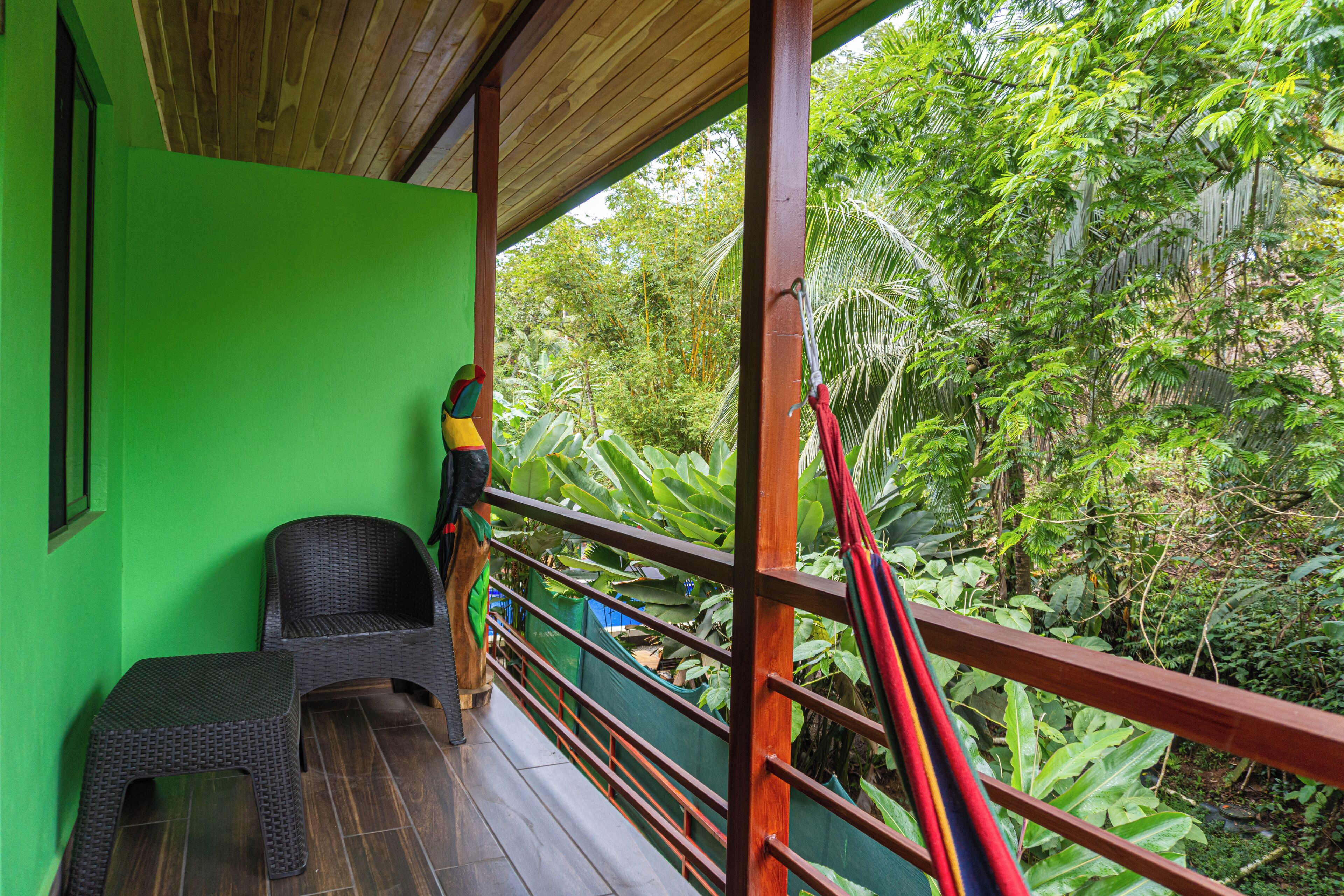 A balcony with wicker furniture, a green wall, and a view of dense tropical foliage.