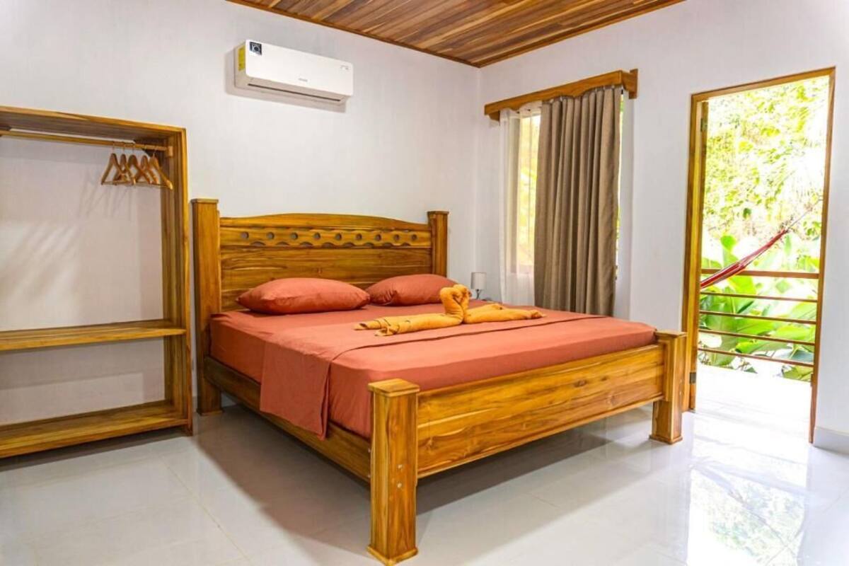 Ein Bett mit Holzbettgestell, einer roten Bettdecke und Kissen, ein Holzschrank und ein Fenster mit Vorhängen.