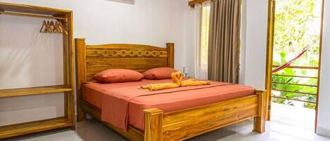 Una cama de madera con colcha y almohadas rojas, un armario de madera y una ventana con cortinas.