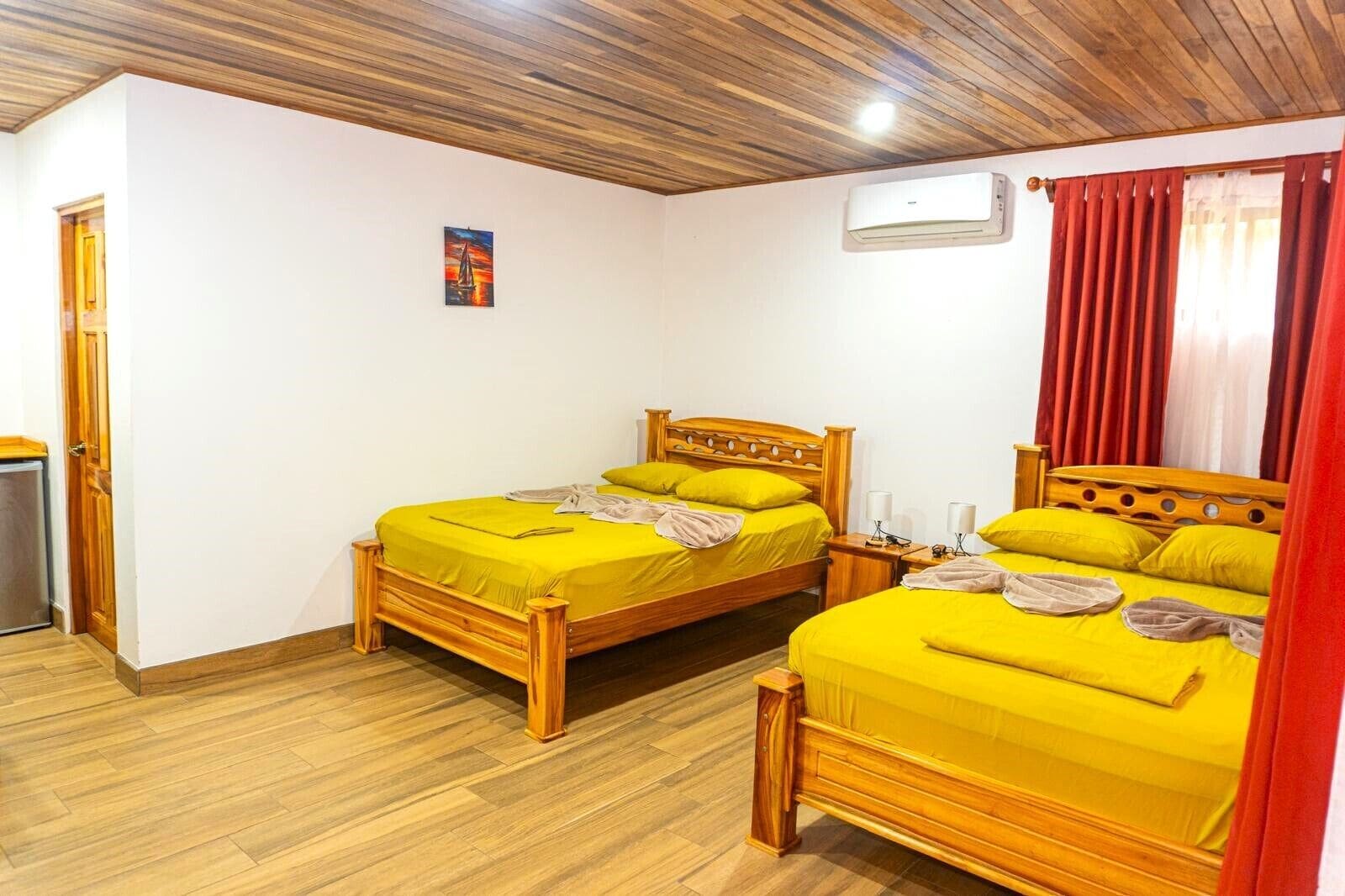 A room with two wooden beds, a wooden ceiling, and a small air conditioning unit.