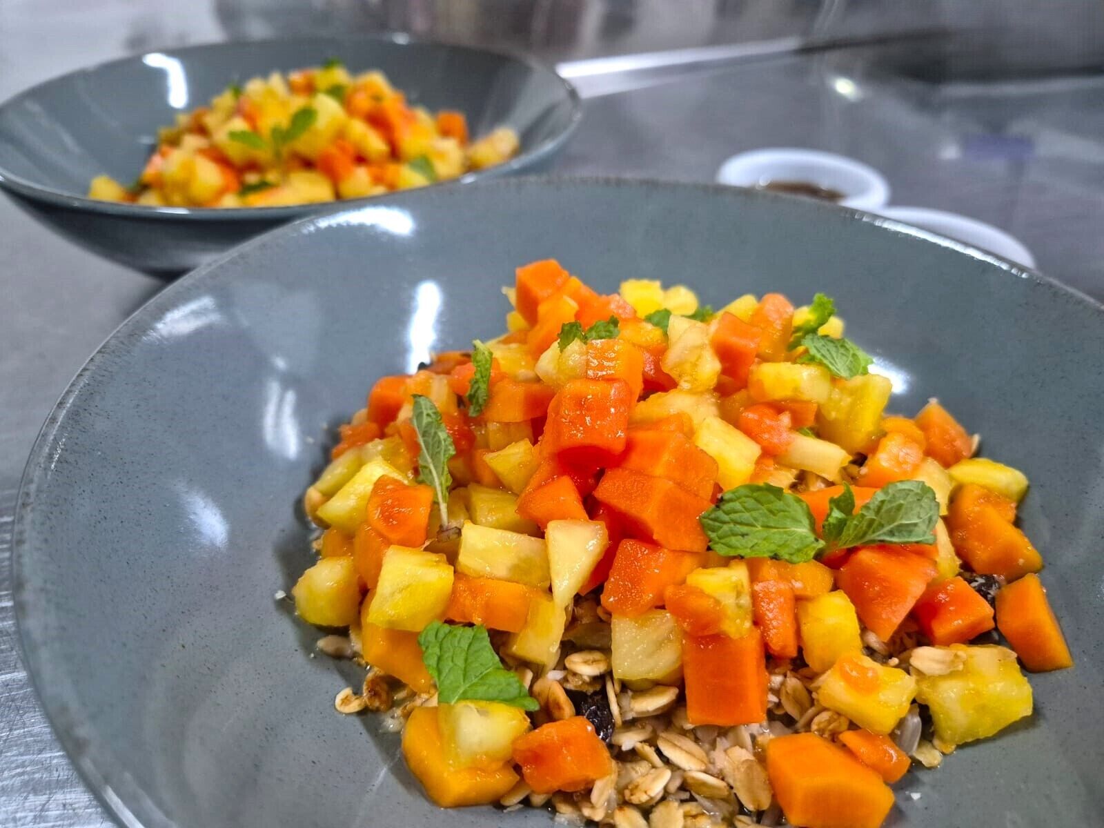 Een schaal met blokjes mango en wortelen, versierd met muntblaadjes.
