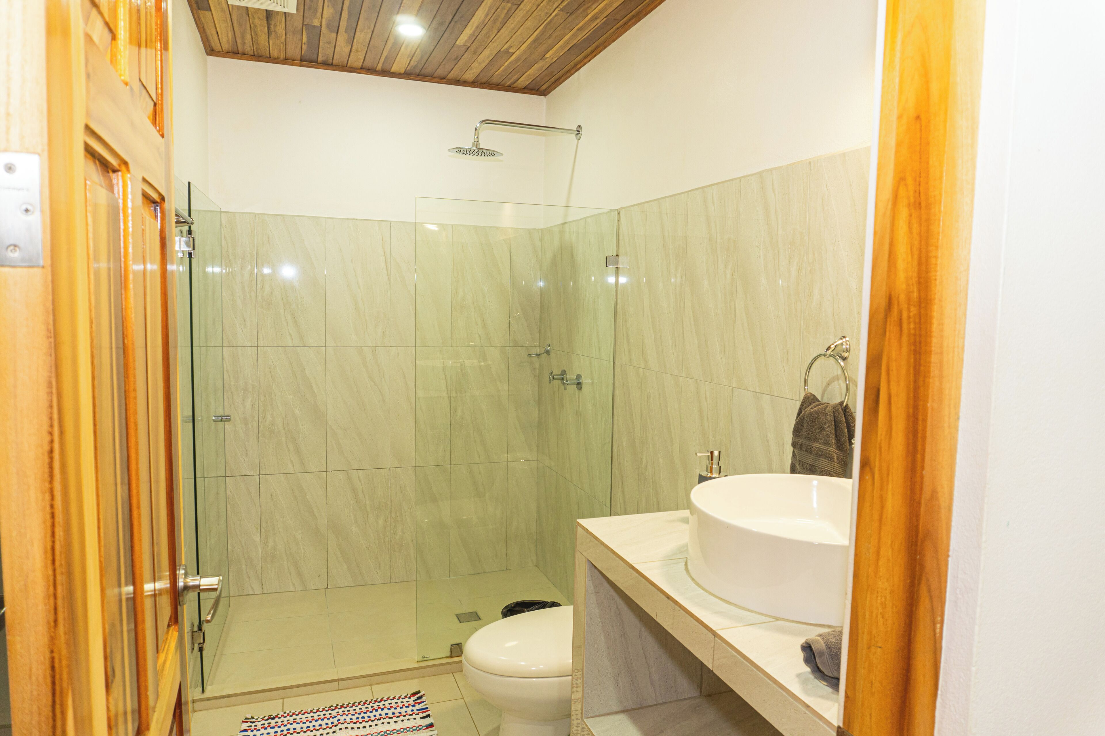 A modern bathroom with a glass-enclosed shower, a white sink, and a wooden ceiling.