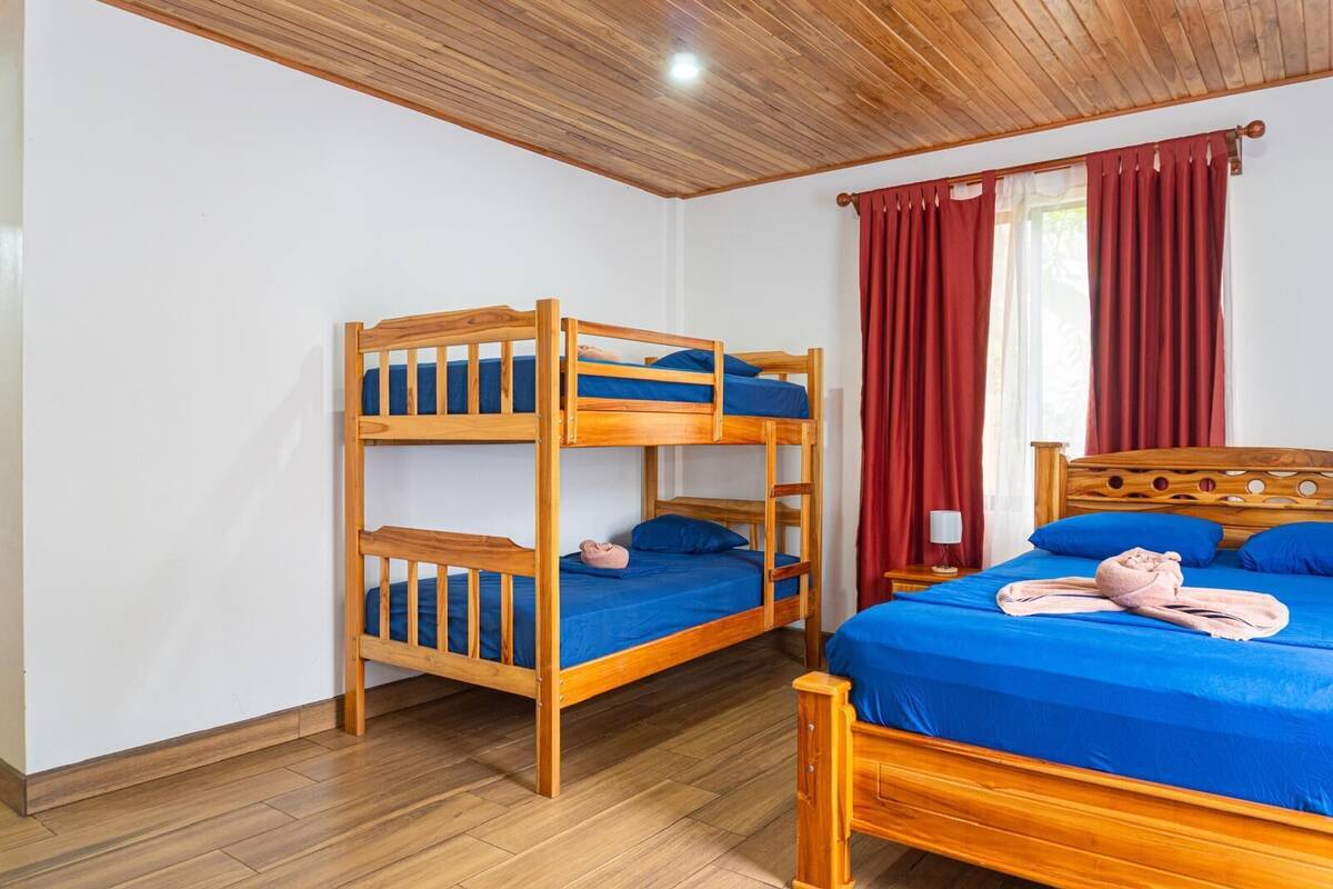 Ein Zimmer mit einem Etagenbett, einem Einzelbett, Holzboden und roten Vorhängen.