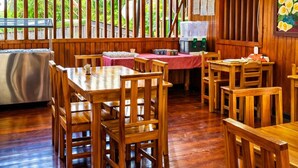A wooden interior with a ceiling fan, dining tables, chairs, and a view through the windows. - CORCOVADO & DRAKE INN (Drake Bay)