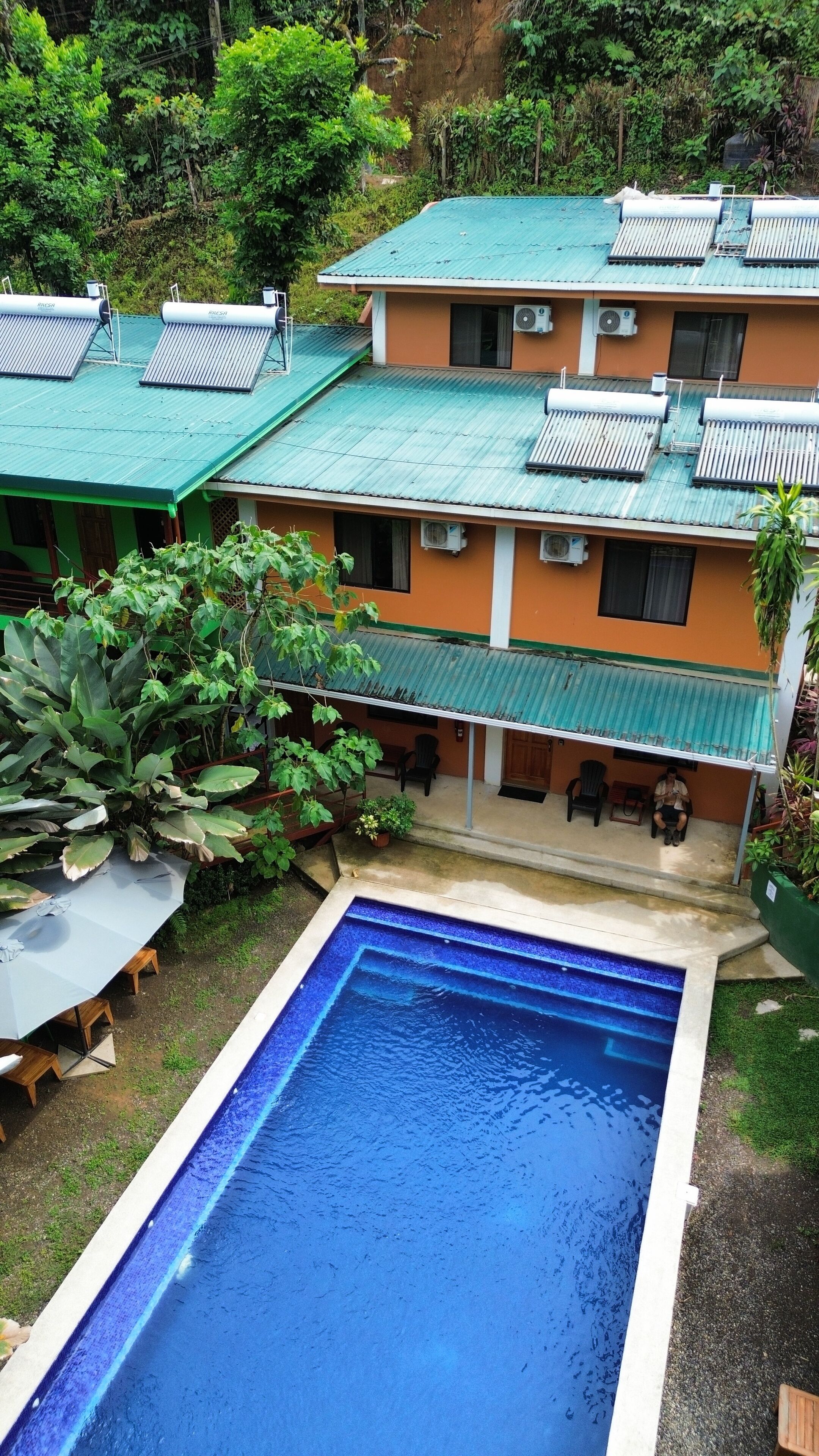 A building with a swimming pool, solar panels, and a covered patio area.