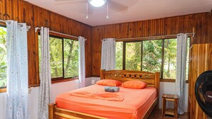 A wooden-paneled room with a bed, curtains, and a window. - CORCOVADO & DRAKE INN (Drake Bay)