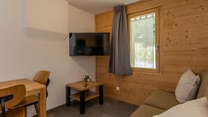 A compact living space with a wooden interior, a flat-screen TV mounted on the wall, a small table with a chair, and a sofa. - ARNICA - PUSSY LA LECHERE (PUSSY LA LECHERE)