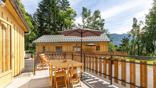 A wooden cabin with a tiled roof, a balcony with a table and chairs, and a view of mountains. - ARNICA - PUSSY LA LECHERE (PUSSY LA LECHERE)