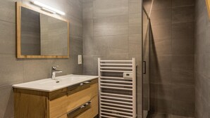 A modern bathroom with a wooden vanity, a white sink, a mirror, and a walk-in shower. - ARNICA - PUSSY LA LECHERE (PUSSY LA LECHERE)