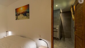 A bedroom with a bed, a bedside table, a lamp, and a painting of a mountain landscape. - ARNICA - PUSSY LA LECHERE (PUSSY LA LECHERE)