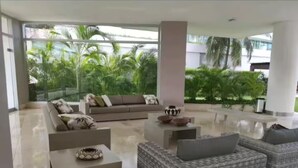A spacious living area with a large sofa, two armchairs, and a coffee table. There is a view of lush greenery outside through large windows. - First line beach in Cartagena edif.morros 3 (Cartagena)