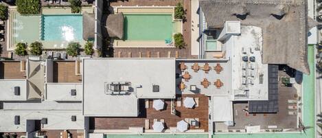 An aerial view of a rooftop with a swimming pool, outdoor seating area, and a tennis court.