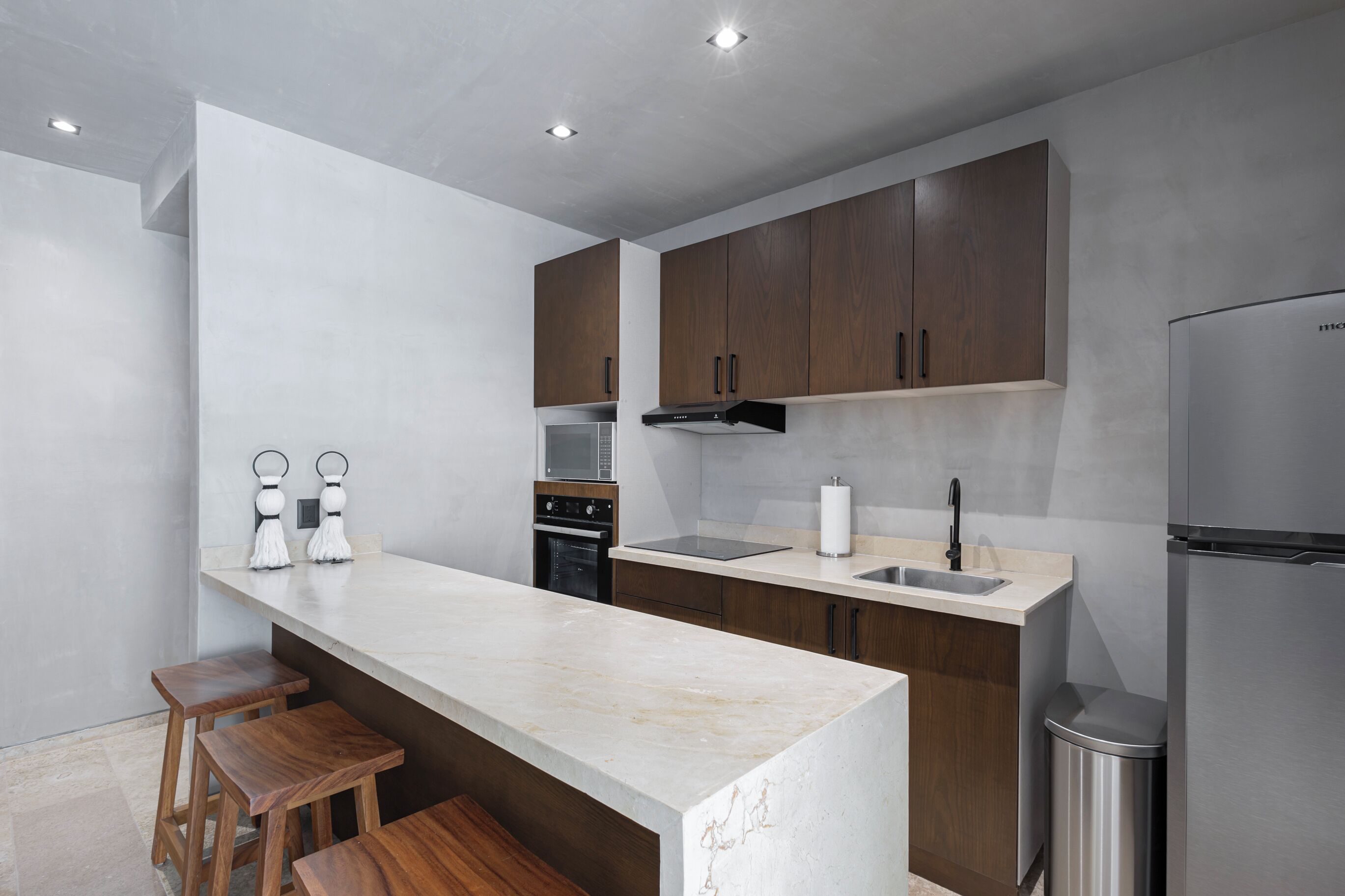 A modern kitchen with a marble countertop, wooden cabinets, stainless steel appliances, and a trash can.