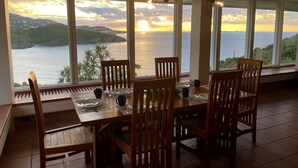 A dining area with a table set for four, large windows offering a view of the sea and hills. - H2O Eco Villa (ST Thomas)