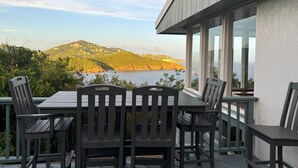 A deck with a table and chairs overlooking a scenic view of a lake and hills. - H2O Eco Villa (ST Thomas)