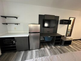 Habitación de hotel compacta con kitchenette, un televisor de pantalla plana, una silla y un espejo.