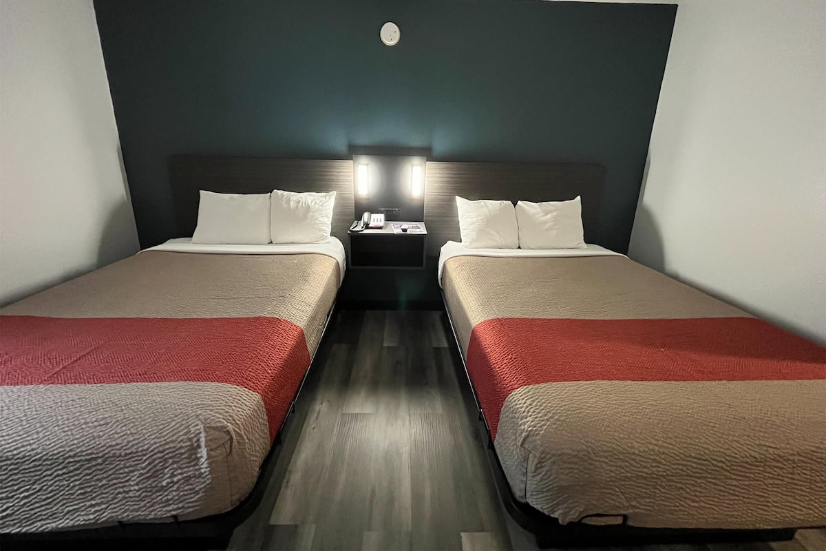 Ein Hotelzimmer mit zwei Betten, einem Nachttisch mit Telefon und Lampe sowie einer dunkel gefärbten Wand.