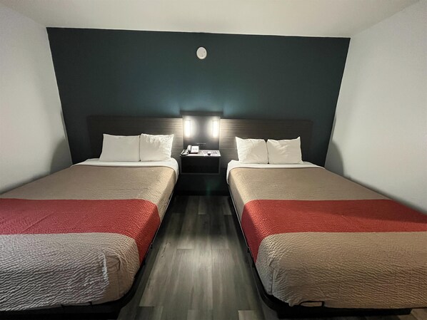 A hotel room with two beds, a nightstand with a phone and a lamp, and a dark-colored wall. - Studio 6 Suites Urbana, IL (Urbana)