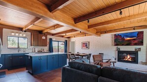 A modern kitchen with blue cabinets, a dining area with a fireplace, and a living room with a large sofa.