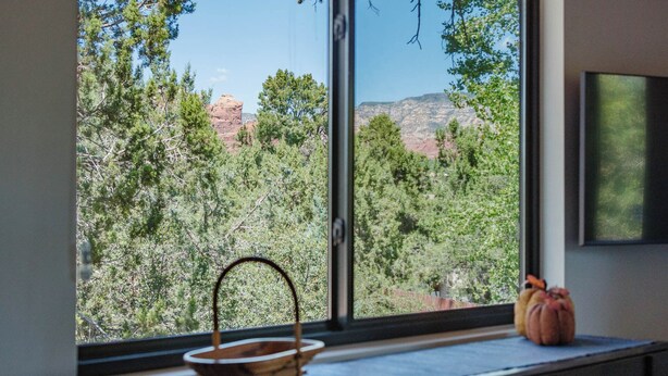 A window with a view of red rock formations and trees.