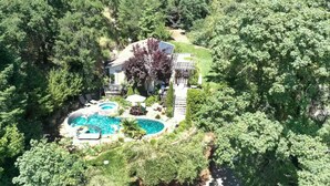 A house surrounded by dense forest with a swimming pool and outdoor seating area.