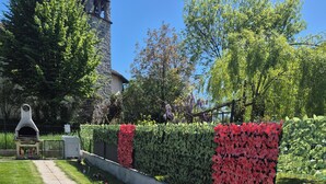 A garden with a pathway, a barbecue area, and a stone wall with red flowers.