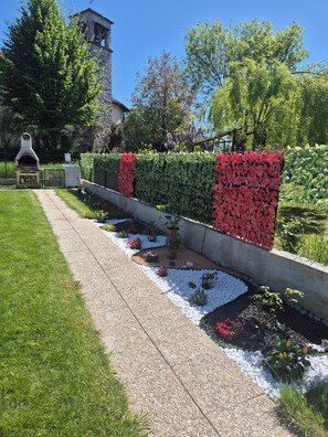 A garden with a pathway, a barbecue area, and a stone wall with red flowers.