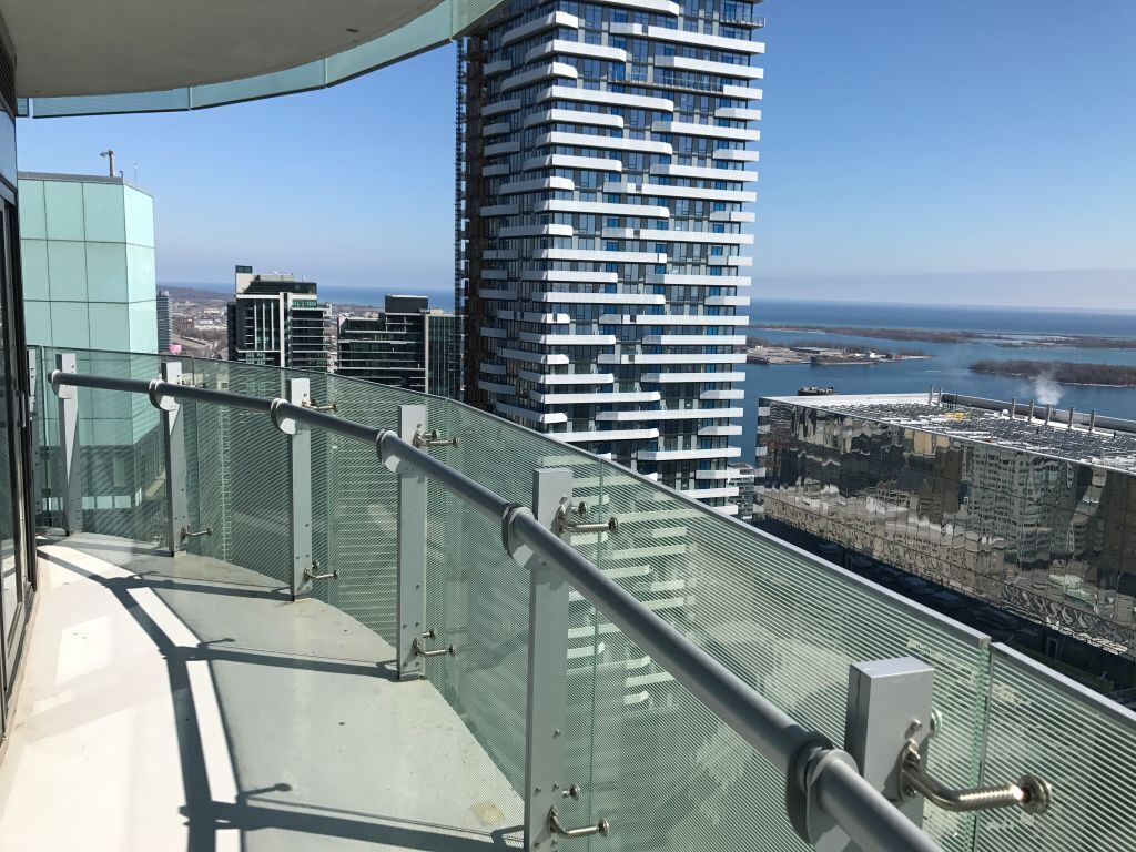 A high-rise building with a modern design, featuring a glass balcony railing and a view of the city and coastline.